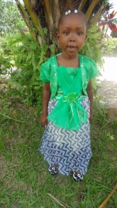 A young girl in green and white dress standing next to tree.