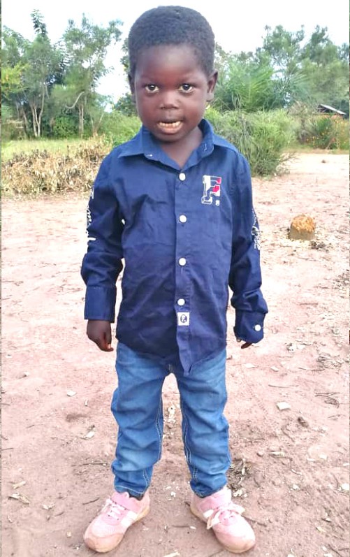 A young boy standing in the dirt wearing jeans and a blue shirt.