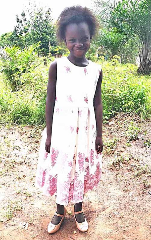 A young girl standing in the dirt wearing a dress.