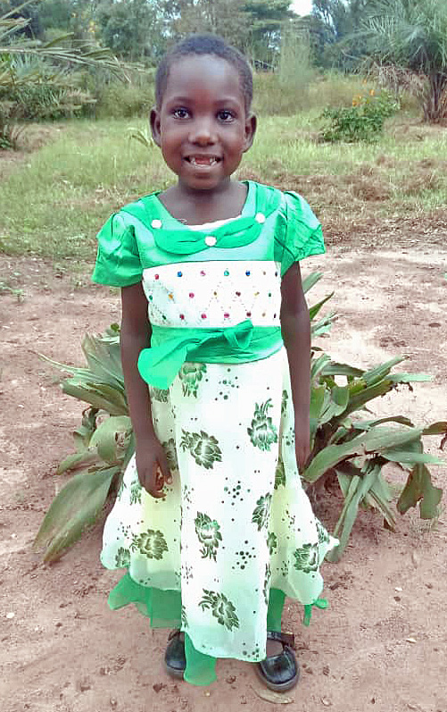 A young girl in green dress standing next to plants.
