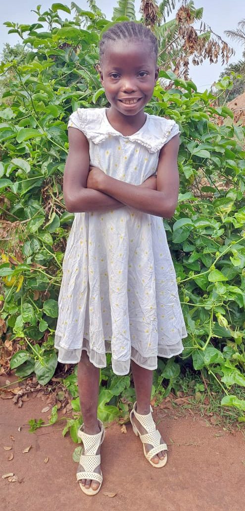 A girl in white dress standing next to green bushes.